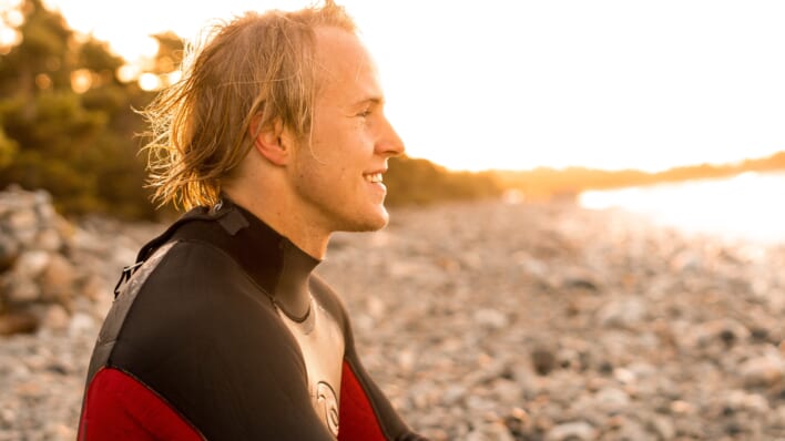 young man sits in wetsuit on the beach