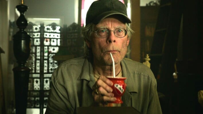 Stephen King in cap drinking out of a straw.